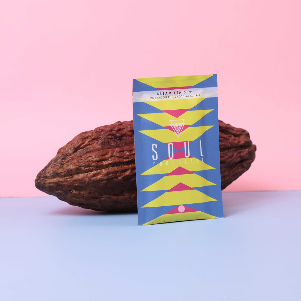 Assam tea Soul chocolate bar packaging with a cocoa bean on a pink and blue gradient background