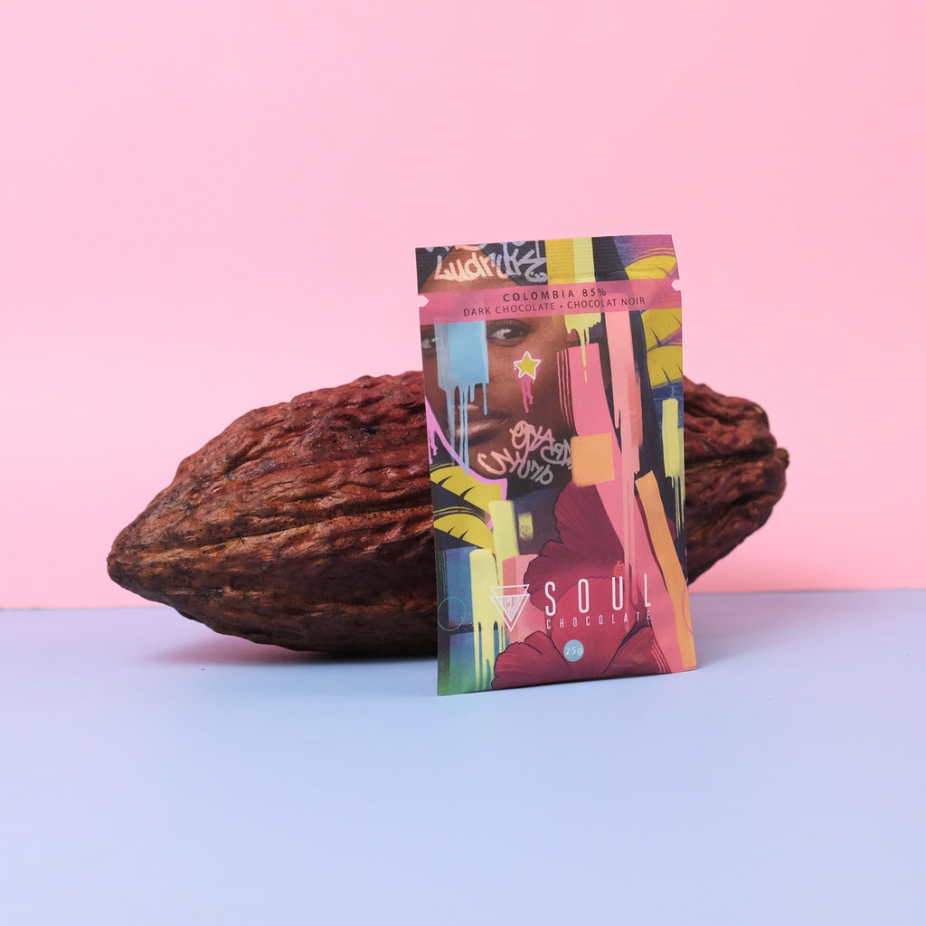 Colorful chocolate bar package resting on a cacao pod on a pink and blue gradient background