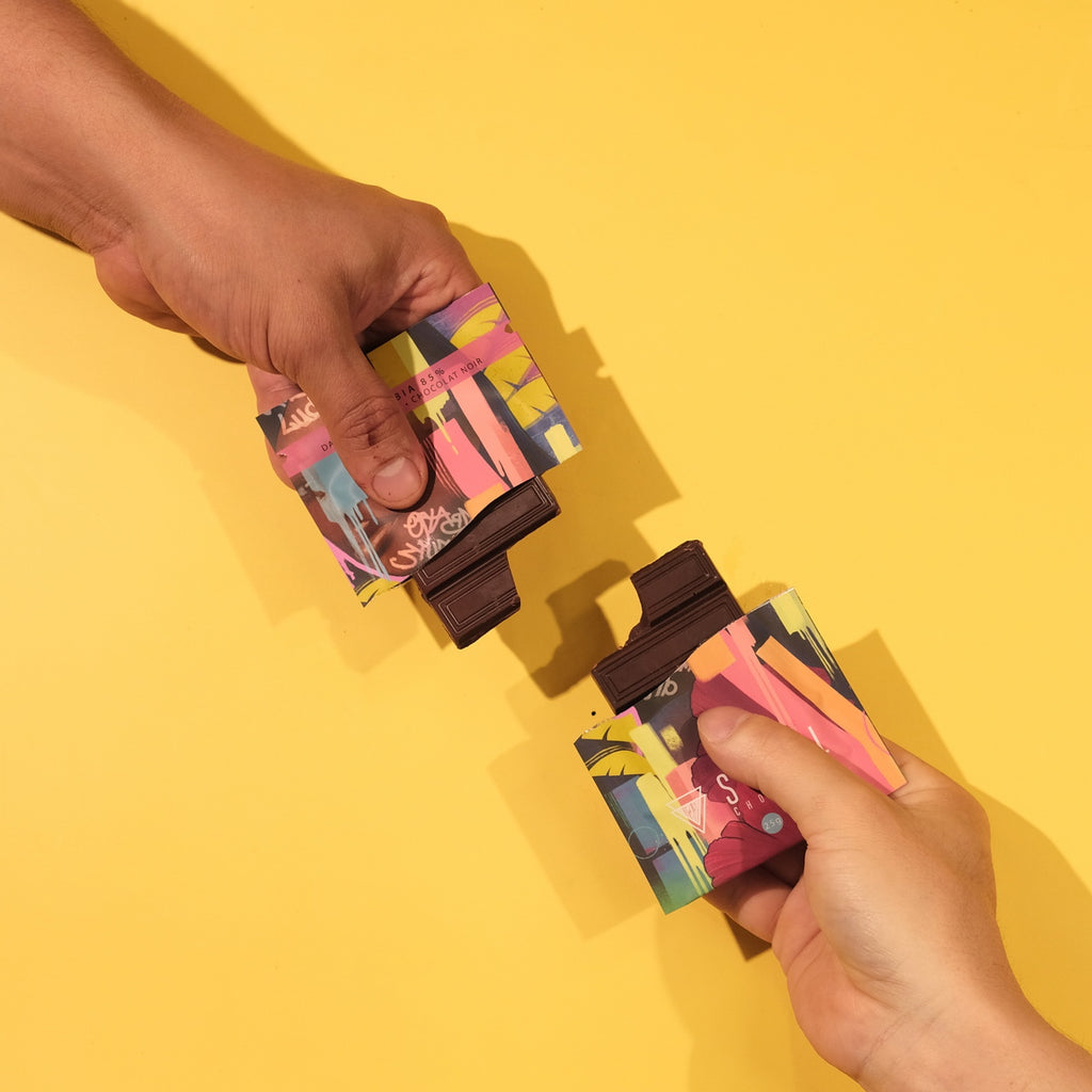 Two hands holding colorful colombian dark chocolate against a yellow background