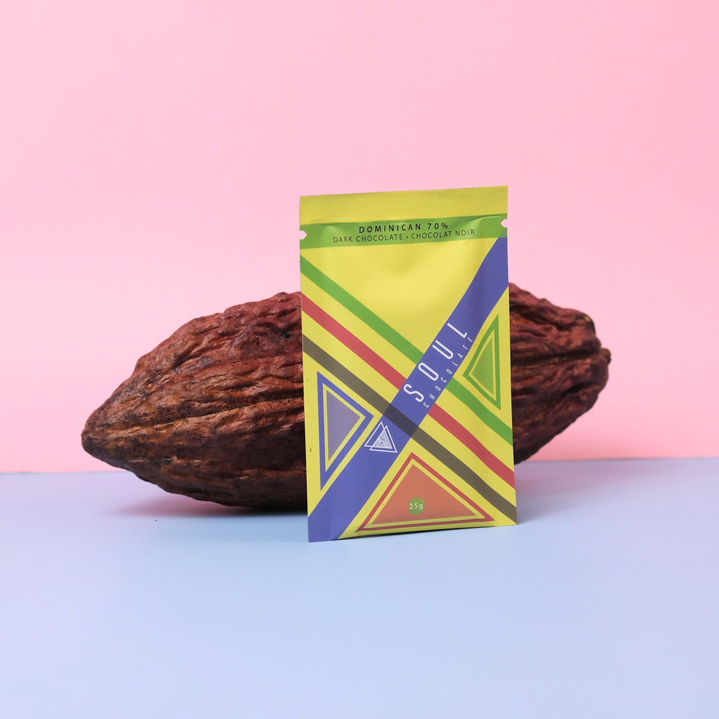 Colorful dominican origin chocolate packaging with geometric design in front of a cocoa bean on a pink and blue gradient background