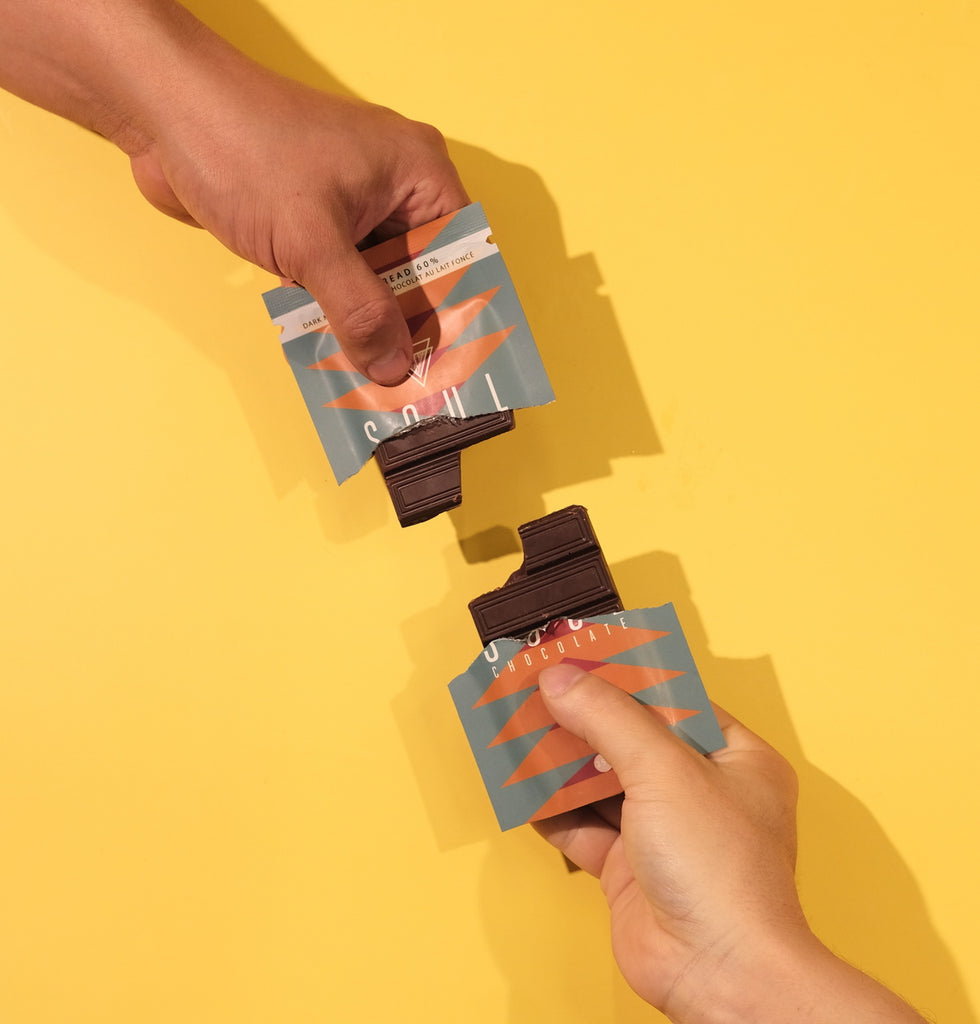 Two hands holding small packets of gingerbread chocolate on a yellow background