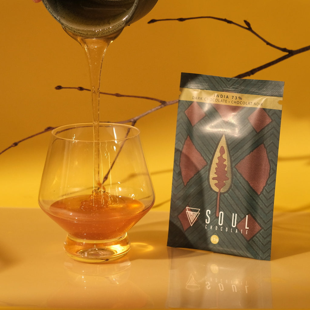 Tea being poured into a glass with a 'Soul Chocolate' package of India 73% dark chocolate on a yellow background