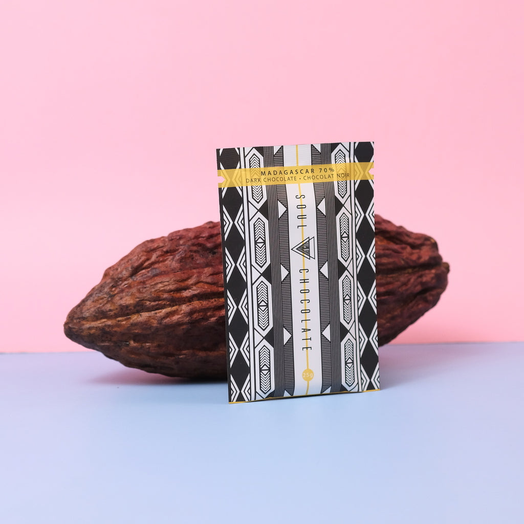 Chocolate bar package of Madagascar chocolate with geometric design in front of cocoa beans on a pink and blue gradient background
