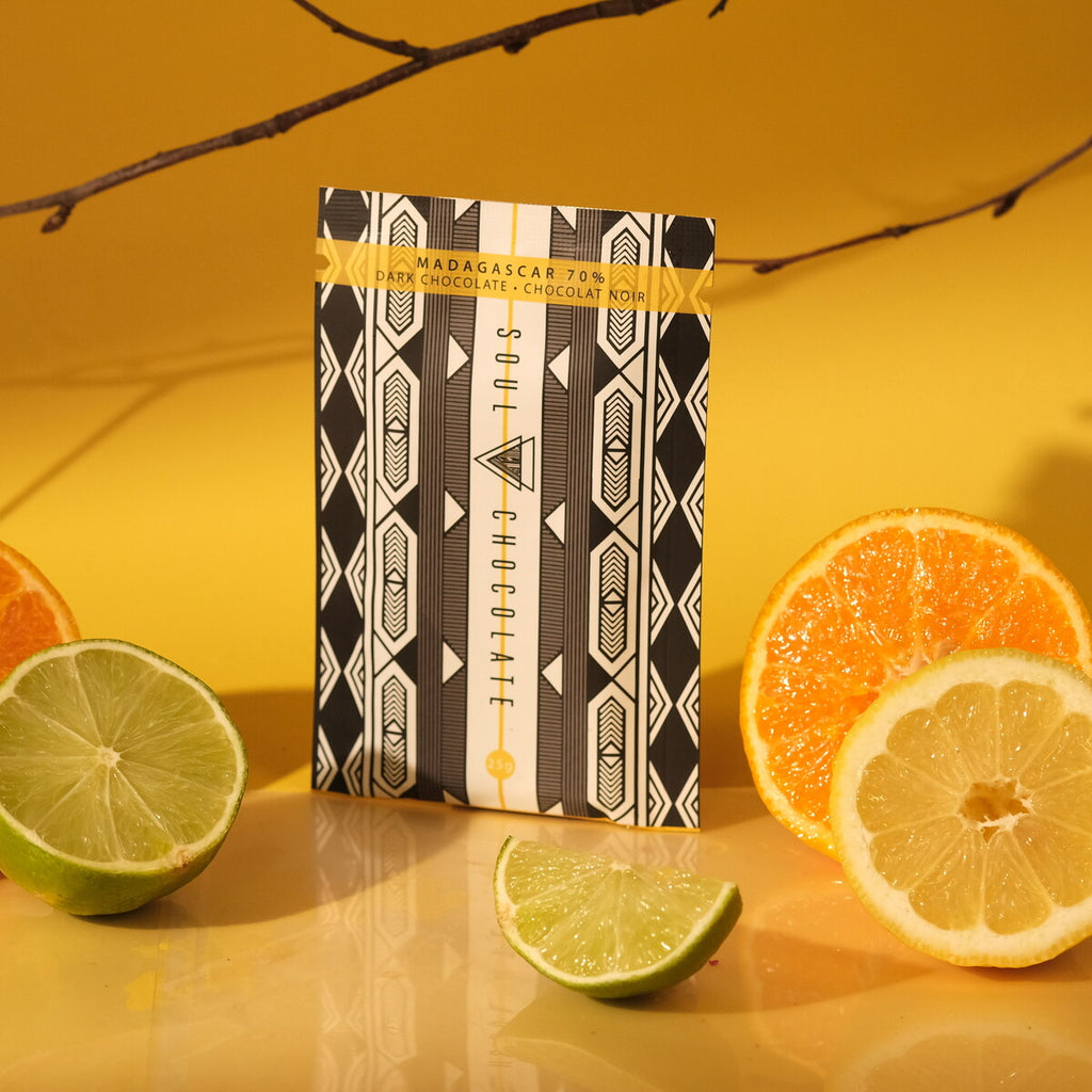 Chocolate bar from Madagascar with a patterned wrapper surrounded by citrus fruits on a yellow background