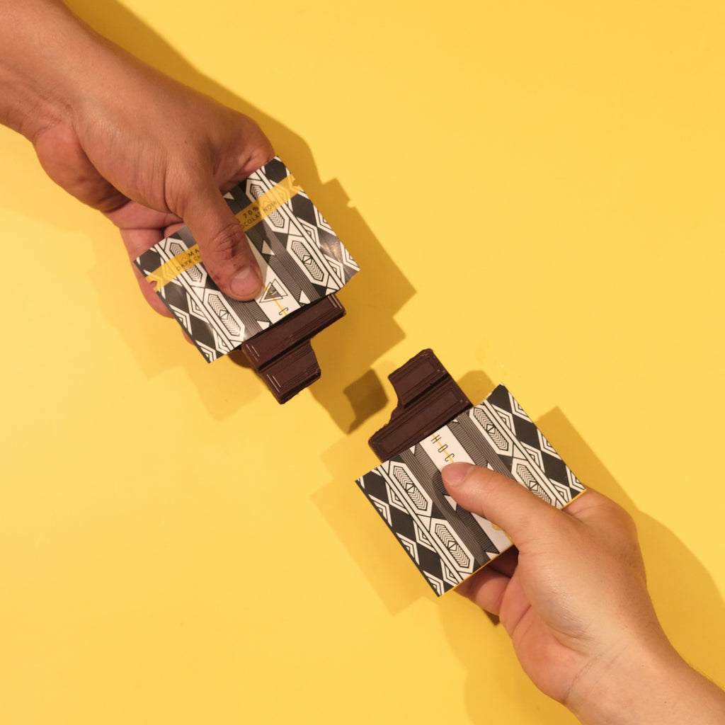 Two hands holding checker patterned chocolate bars against a yellow background
