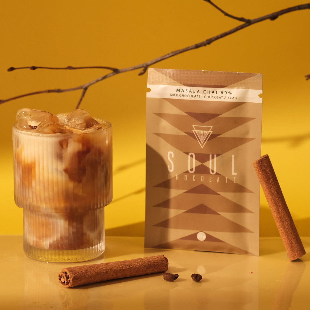 Glass of iced chai with a package of Soul Chocolate Masala Chai on a yellow background with cinnamon