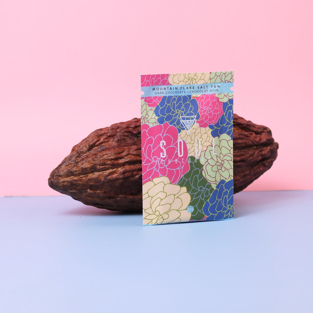 A floral package of flake salt dark chocolate leaning against a large cacao pod