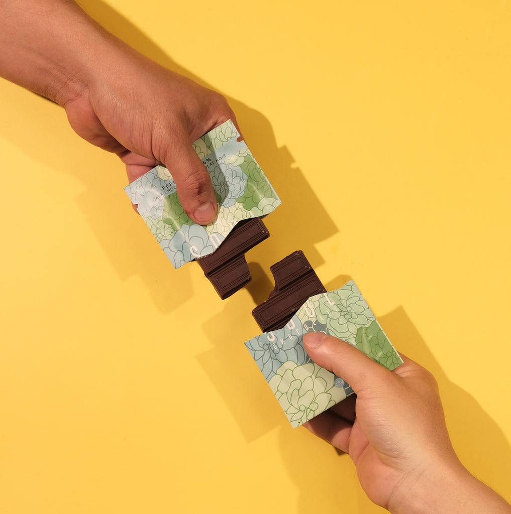 Two hands holding floral-patterned green peppermint chocolate on a yellow background