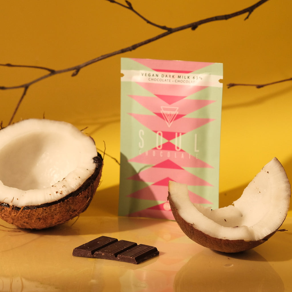 Vegan dark milk chocolate bar with a fresh coconut and chocolate packaging on a yellow background