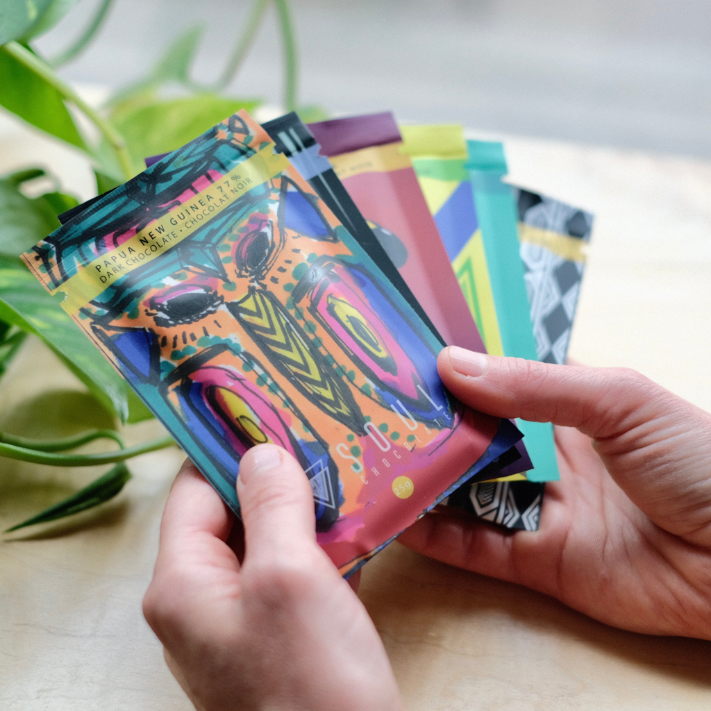a pair of hands holds a splayed arrangement of wrapped chocolate bars from a collection of organic single-origin craft chocolates